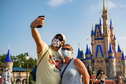 A couple at Disney World taking a selfie in protective masks, one of which is Mickey Mouse-themed 