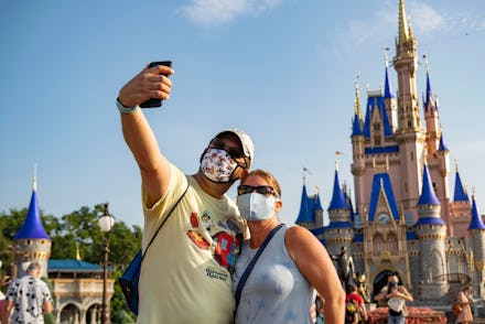 A couple at Disney World taking a selfie in protective masks, one of which is Mickey Mouse-themed