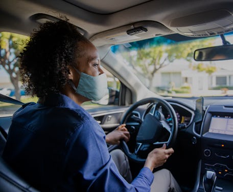 A person drives a car while wearing a mask.
