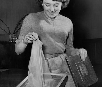 A woman can be seen lifting nylon out of a box while smiling. The photo is black and white.