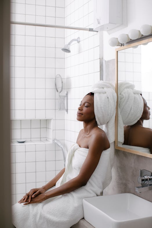 A young Black woman relaxes in her bathroom after taking a bubble bath.