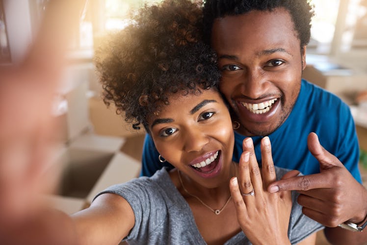 A happy couple takes a selfie showing off their engagement ring. 