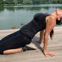 A person performs a backbend outside along a waterfront. Certain yoga flows are especially helpful f...