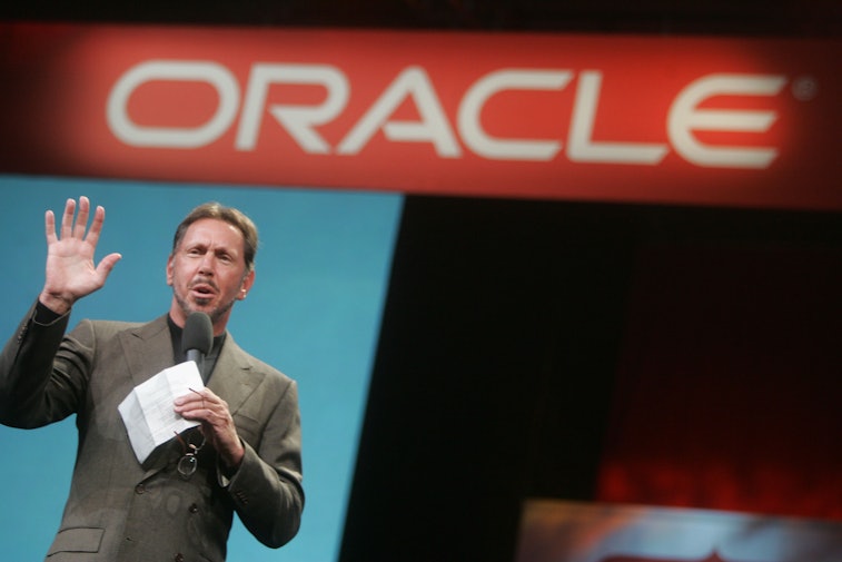 Larry Ellison stands in front of a sign that reads "Oracle."