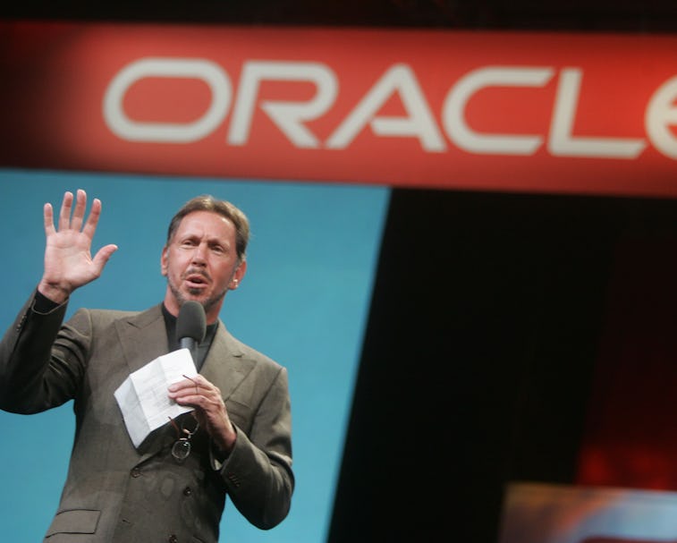 Larry Ellison stands in front of a sign that reads "Oracle."