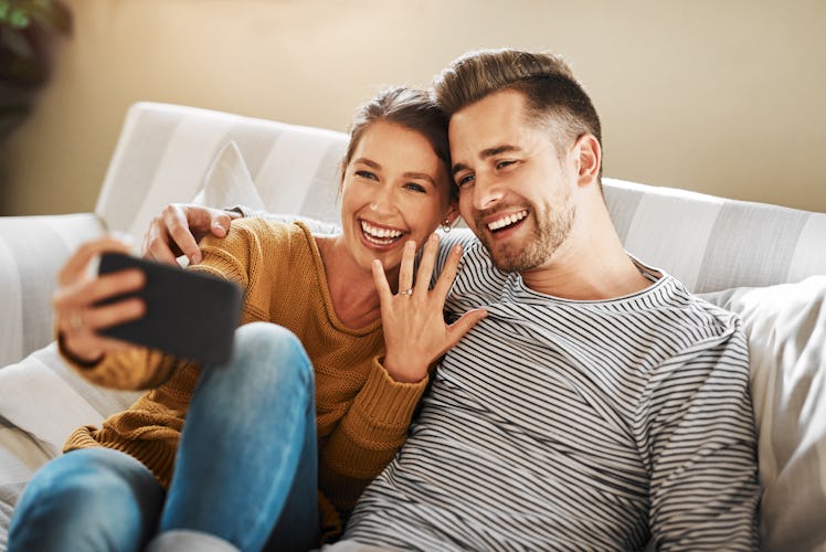 A happy couple takes a selfies, showing off their engagement ring. 