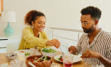 A young Black couple enjoys a fresh meal while sitting at their kitchen table in the summer.