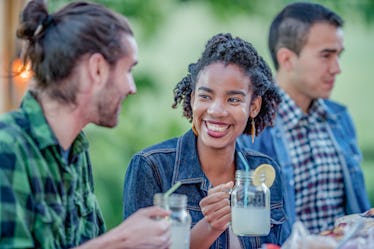 A happy woman smiles at her friend while holding a mason jar filled with lemonade. 