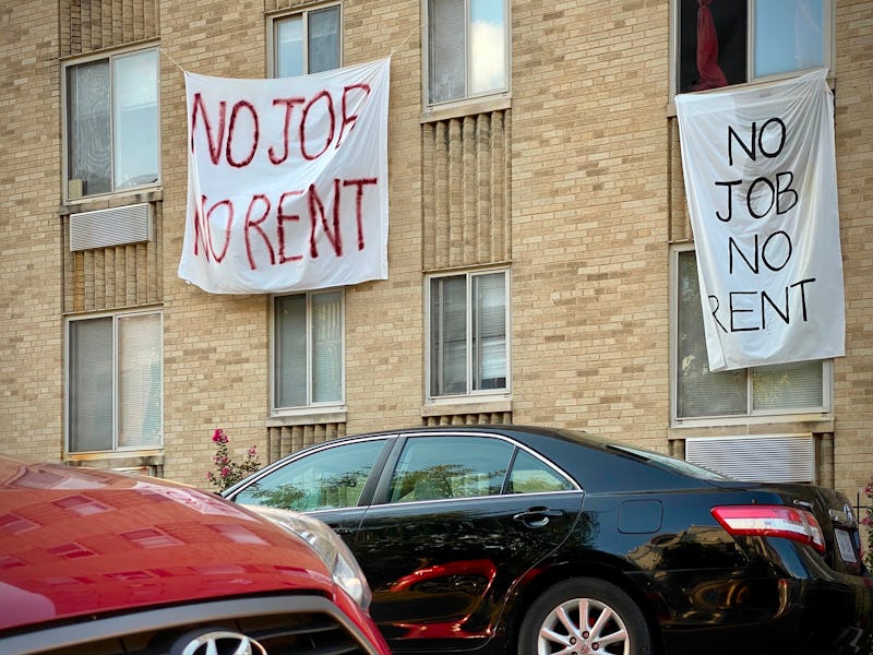 A sign hangs from an apartment window. The letters are written in red paint. It reads: No job, no re...