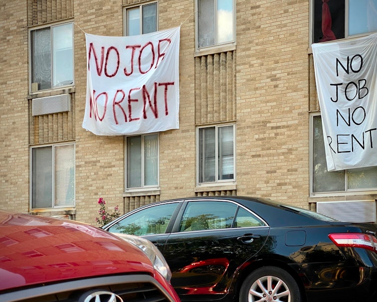 A sign hangs from an apartment window. The letters are written in red paint. It reads: No job, no re...