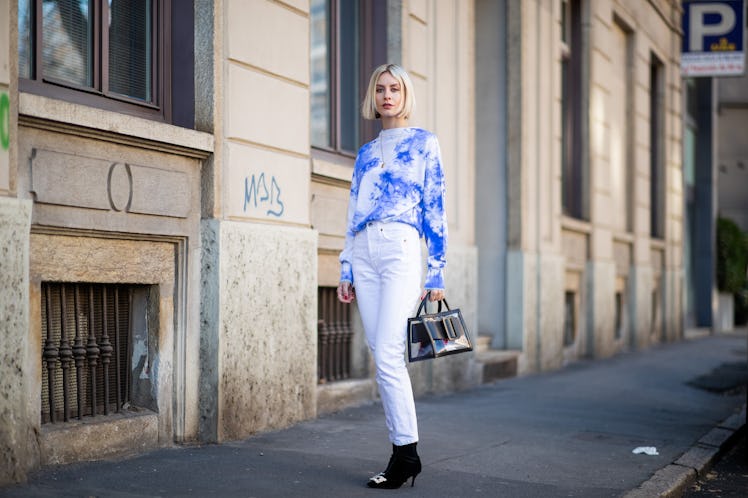 A woman wears a tie-dye sweater, while walking down the street. 