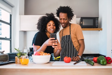 A couple looks at their phone in the kitchen, while cooking together. 
