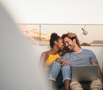 A couple shares a romantic moment while watching a movie on their laptop during sunset, on the rooft...