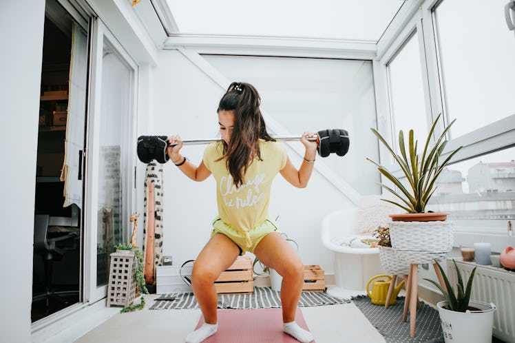 A young woman does weighted squats on the enclosed balcony of her apartment building.