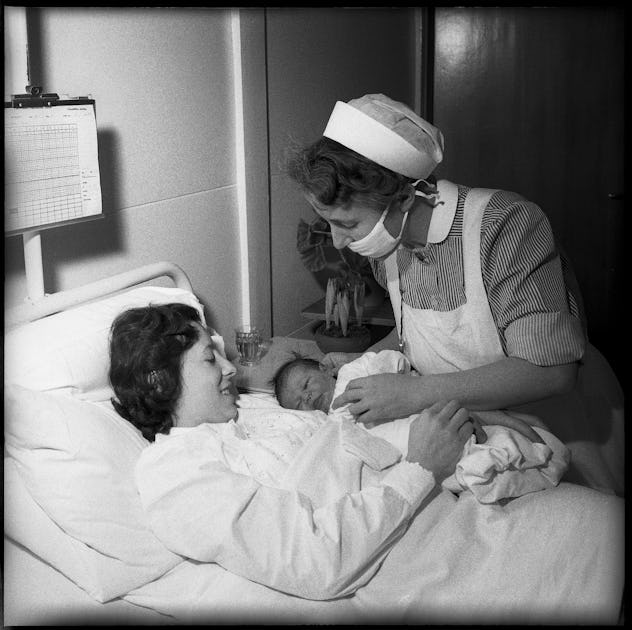 A nurse provides support to a new mom in this vintage maternity ward photo. 