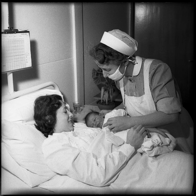 A nurse provides support to a new mom in this vintage maternity ward photo. 