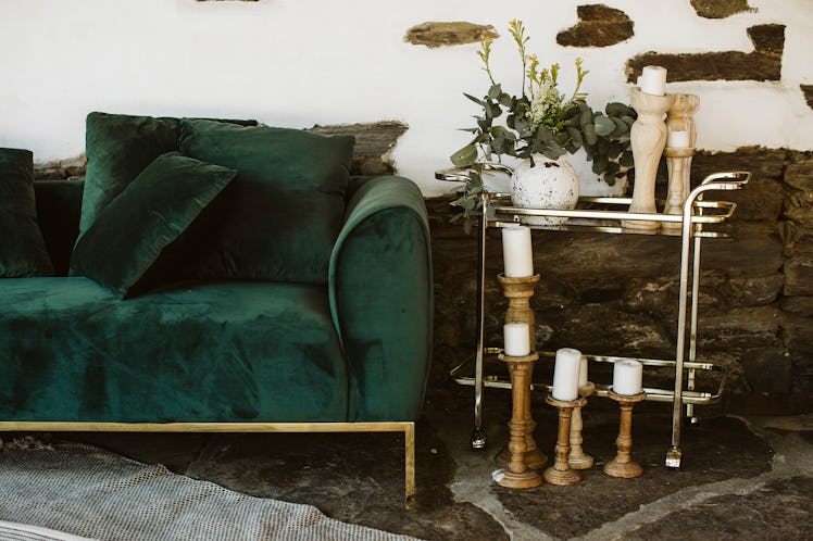 A green velvet couch sits outside against a white brick wall and next to a rack of candlesticks.
