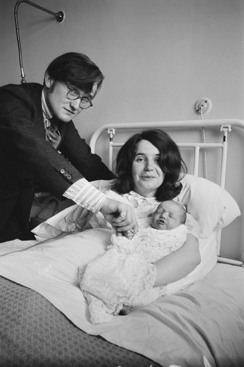 A dad holds his baby's hand as mom cradles the newborn in this vintage maternity ward photo.