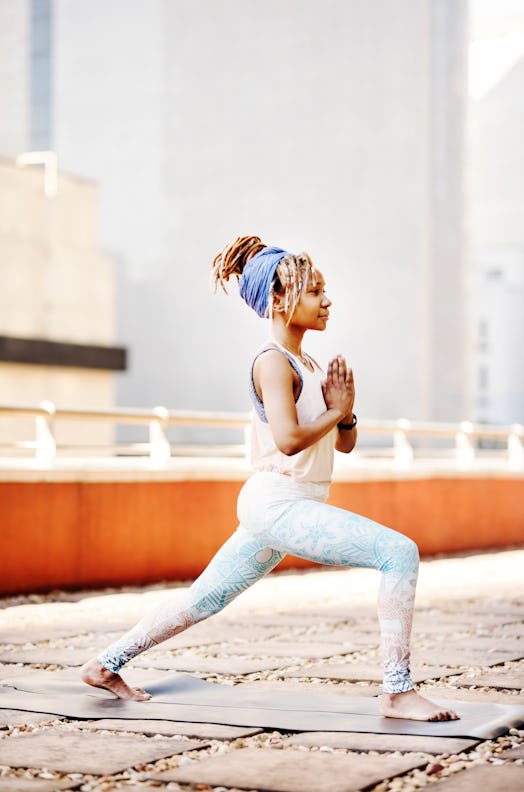 A young Black woman does yoga on the rooftop of her apartment building in the city.