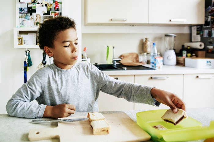 young boy packs sandwich into lunchbox in kitchen