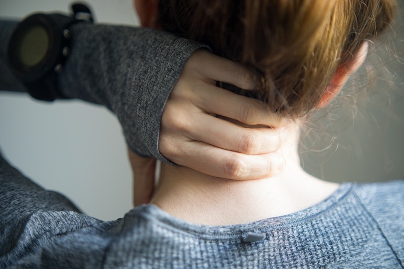 A woman holds her painful neck. Sitting at home can make neck and spine muscles stiff and painful, e...