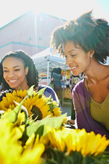Two young Black women shop for sunflowers at the farmer's market in their city.