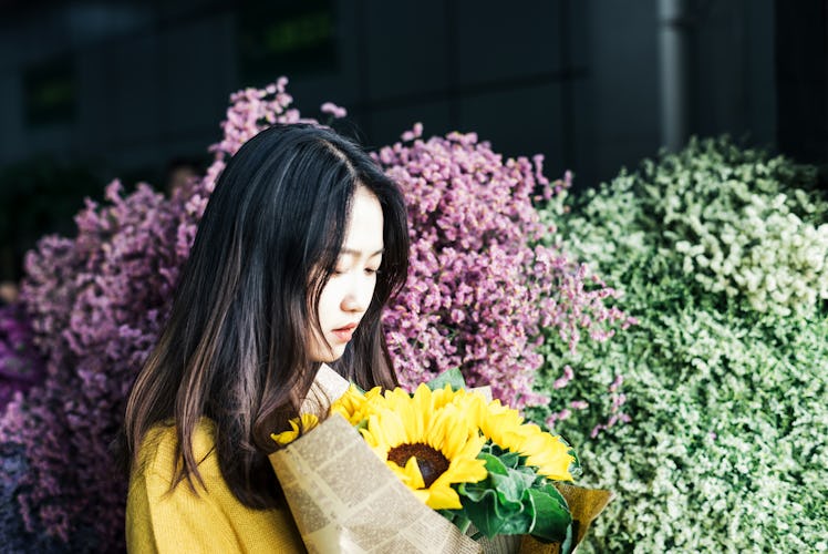 A young Asian woman looks down at a bouquet of sunflowers wrapped in newspaper.