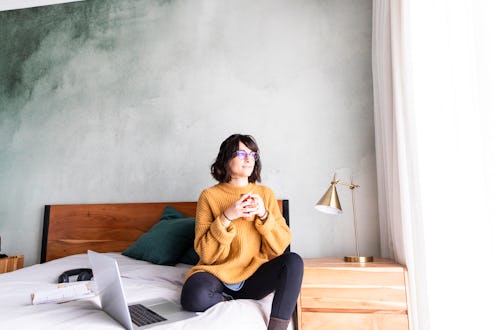 A woman sits in bed with a cup of tea. Does the flu affect your period? OB-GYNs explain how the flu ...