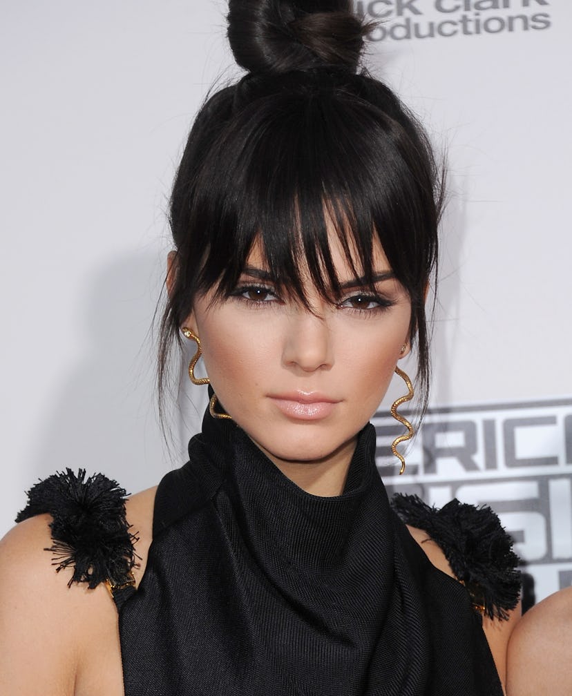 Kendall Jenner with a messy top knot with long bangs and side-pieces out. 