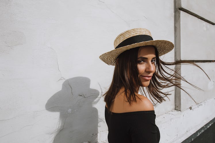 A young woman poses with her shadow in the middle of summer while wearing a hat.