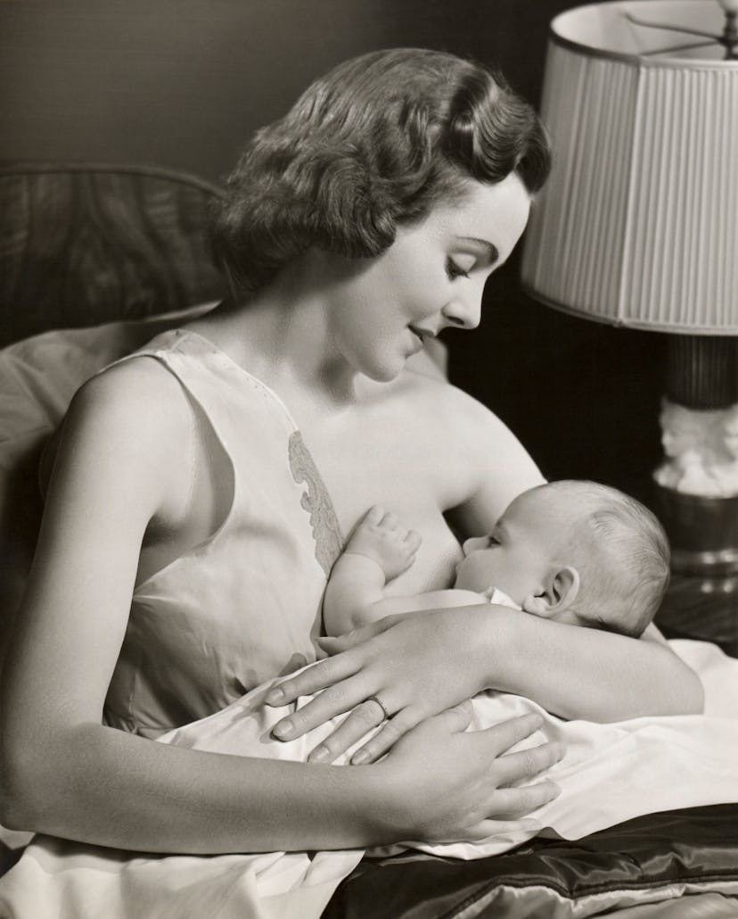 vintage breastfeeding photo of woman breastfeeding baby propped on pillows
