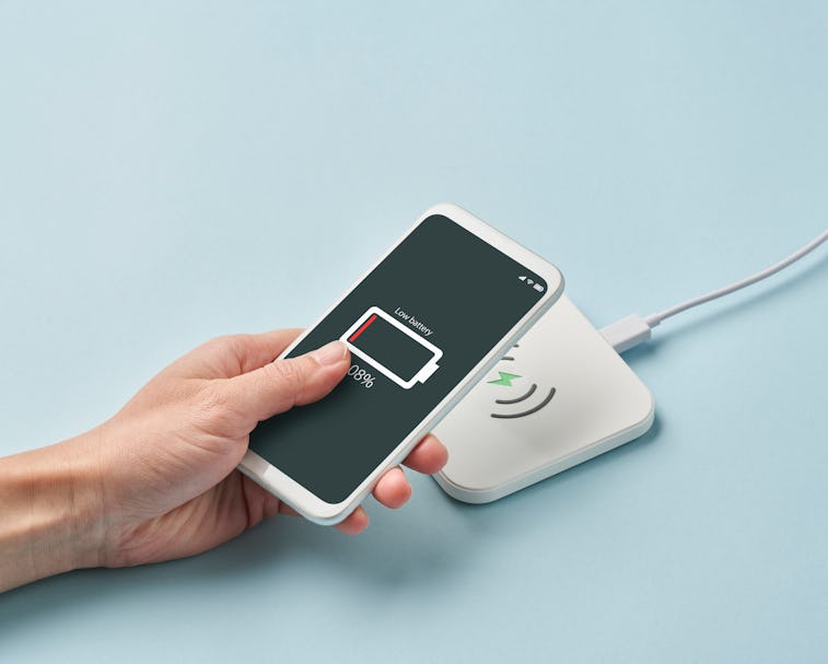 A hand can be seen holding a smartphone. The phone's battery is extremely low and is seen to be char...