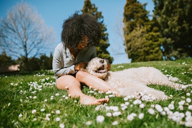 A young Black woman sits in the grass in her backyard with her fluffy dog on a sunny day.
