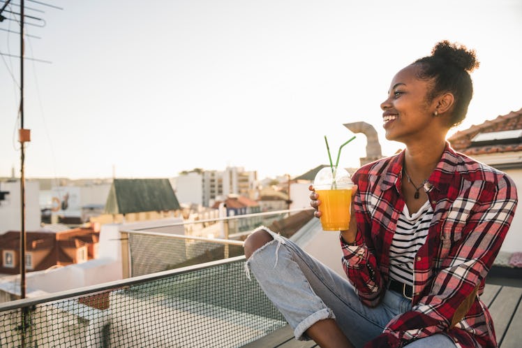 A happy woman watches the sunset from her balcony, while drinking a tea. 