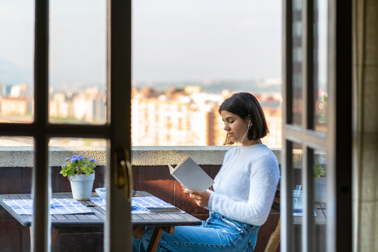 A woman enjoys a quiet moment on her balcony, reading a book and listening to music. 