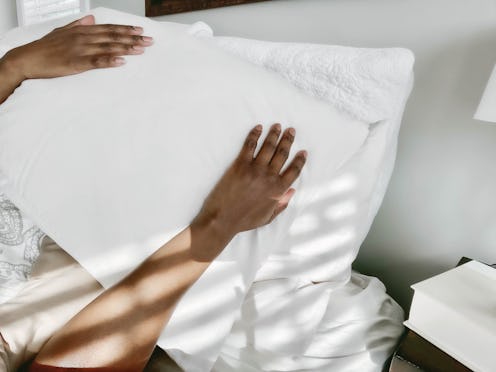 A woman with a pillow over her face tries to sleep. Women explain their quarantine sleep hacks.