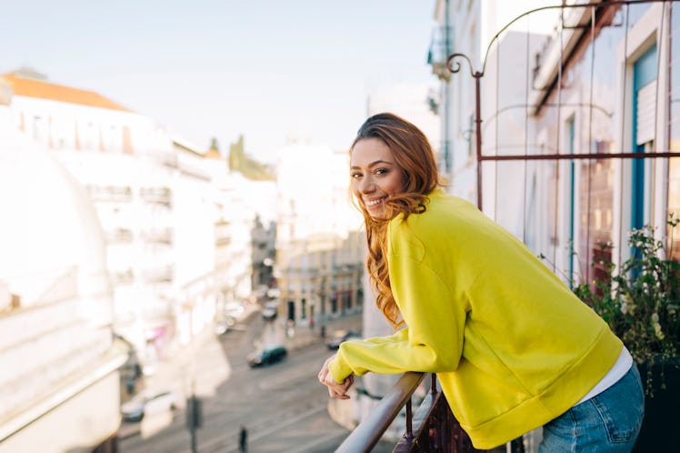 A happy woman in a yellow sweater, enjoys the views from her balcony.