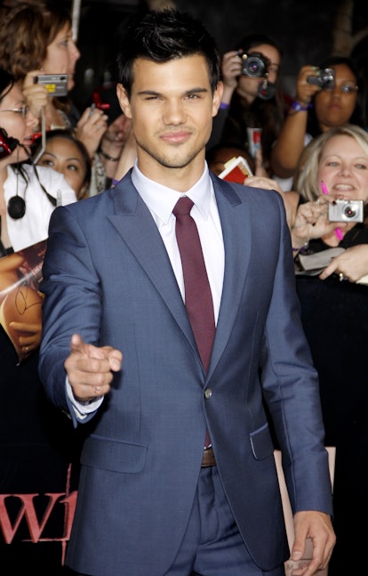 Taylor Lautner stands before a group of 'Twilight' fans, pointing at the camera. He wears a blue sui...