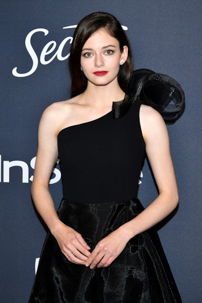 Mackenzie Foy stands with her hands lightly clasped in front of a blue background. She is wearing a ...
