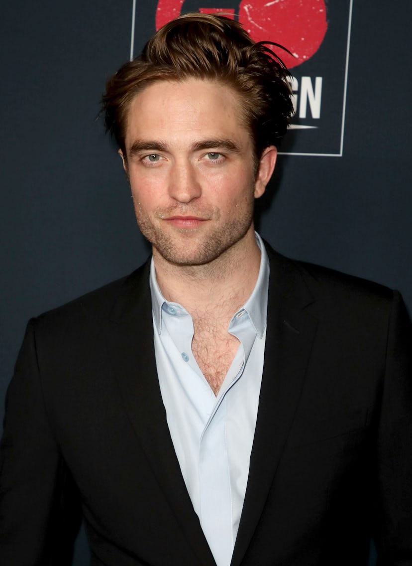 Robert Pattinson looks directly at the camera, wearing a black blazer and grey shirt, unbuttoned at ...