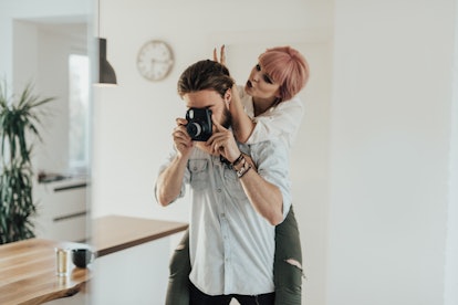 A young couple takes a mirror selfie on their digital camera in a minimalistic home.