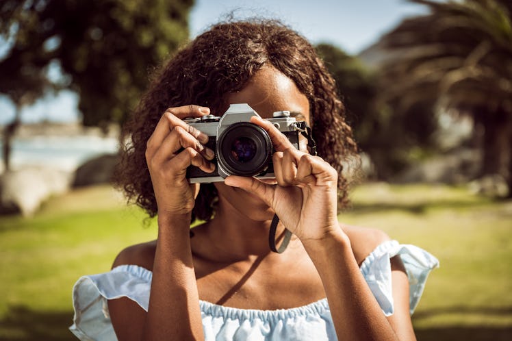 A young Black woman holds up a film camera and uses the zoom ring on a summer day.