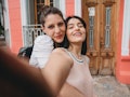 A young lesbian couple poses for a selfie after getting engaged in front of a coral building.