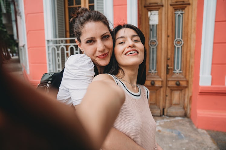 A young lesbian couple poses for a selfie after getting engaged in front of a coral building.