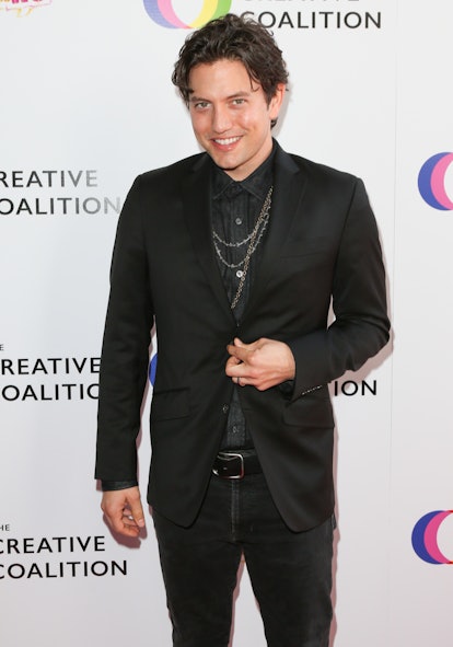Jackson Rathbone stands on the red carpet, smiling. He wears a black suit, a black pinstripe shirt, ...