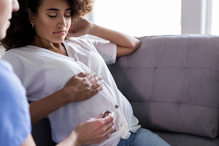 A pregnant woman with Preeclampsia sits on a couch while a doctor does a check up