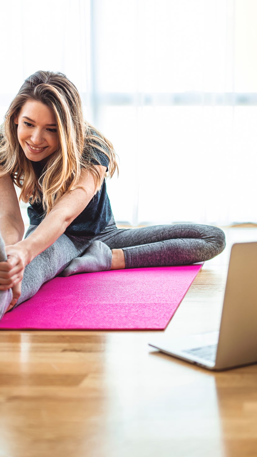 woman stretching on a mat in front of her laptop