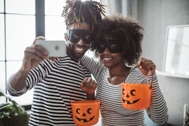 A couple dressed up for Halloween with pumpkin buckets, pose for a selfie on their phone. 