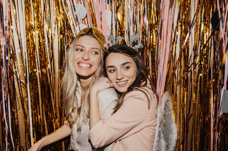 Two young women pose in front of gold streamers while wearing Halloween costumes.