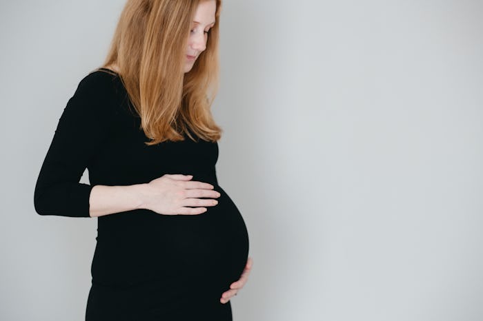 A woman with preeclampsia in a black dress, holding her pregnant belly